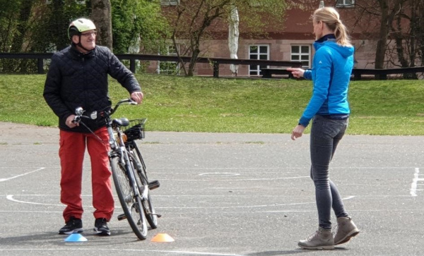 Ein Teilnehmer steht neben einer Trainerin und hält ein Fahrrad, auf einem Übungsgelände für das Forschungsprojekt Sicheres Fahrrad fahren im Alter