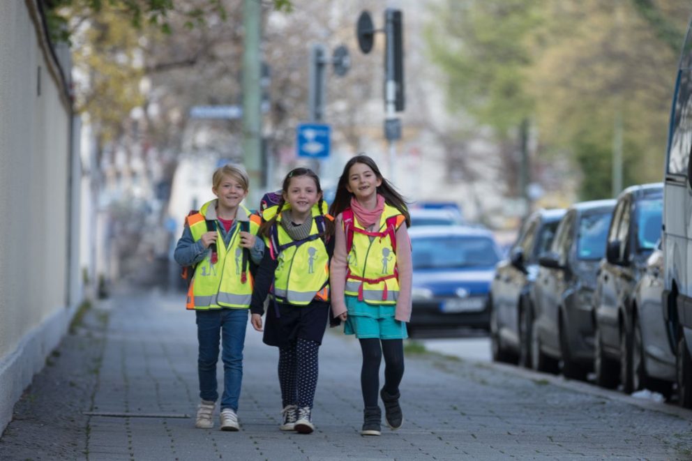 3 Kinder mit reflektierender Warnweste auf dem Schulweg