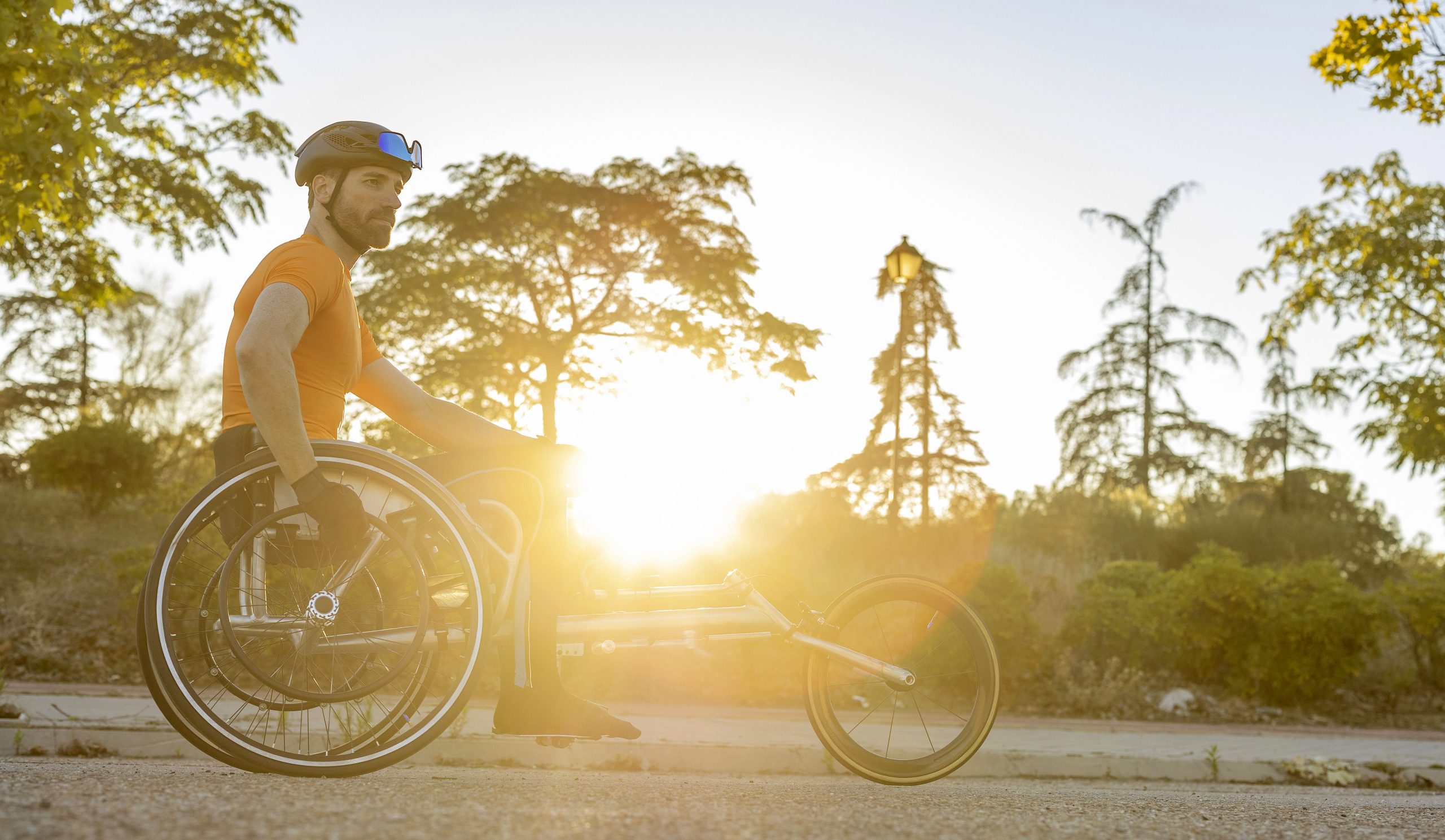 Mann im Rollstuhl, aktiv beim Sport, Natur und Sonne im Hintergrund