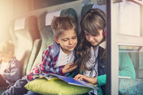 Zwei Kinder sitzen in einer Bahn. Das Mädchen trägt Kopfhörer.