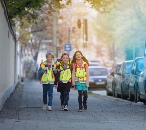 Drei Kinder in Sicherheitswarnwesten auf dem Weg zur Schule