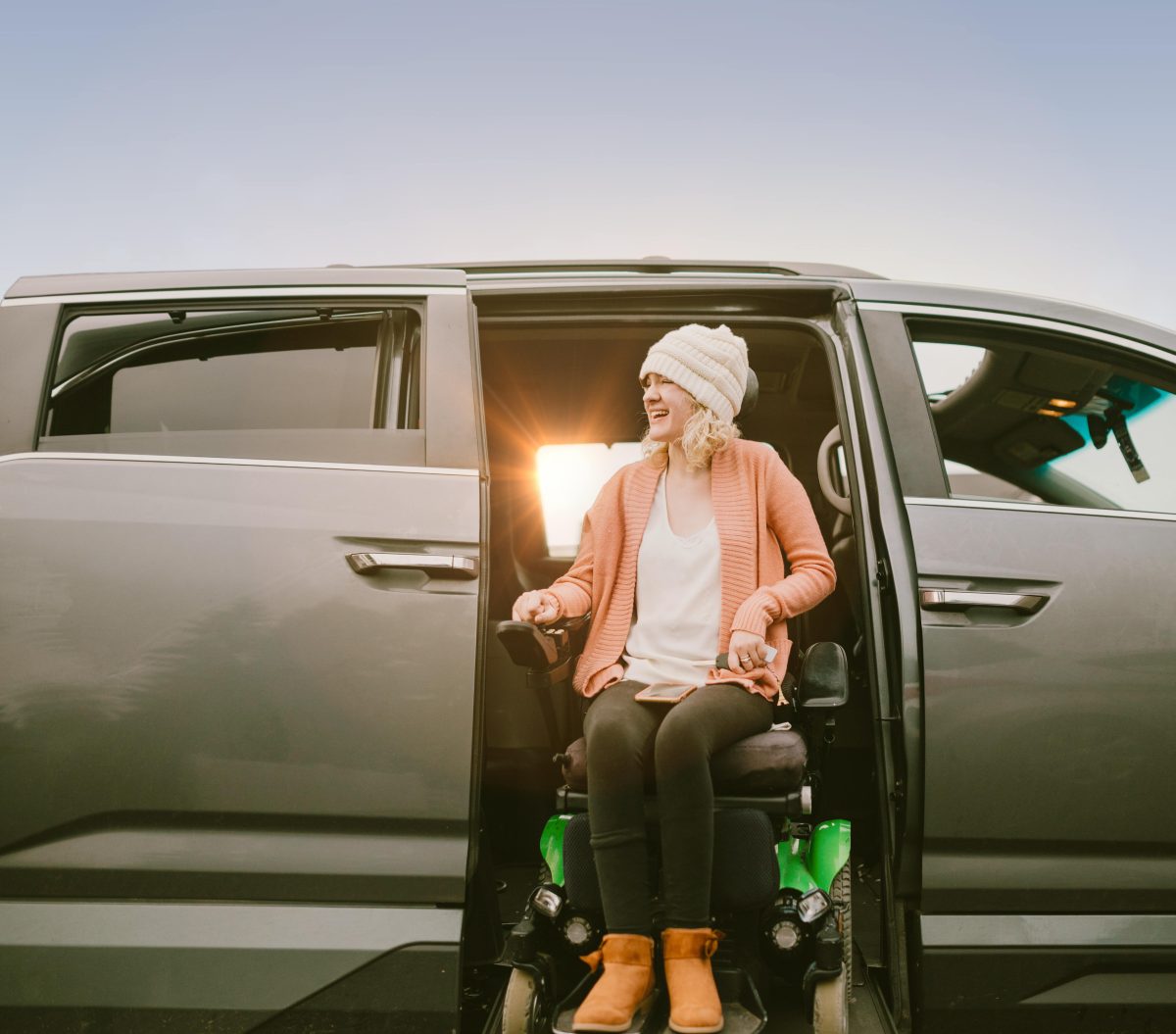 Eine Frau sitzt in einem Auto auf einem Rollstuhl, die Autotüre ist geöffnet