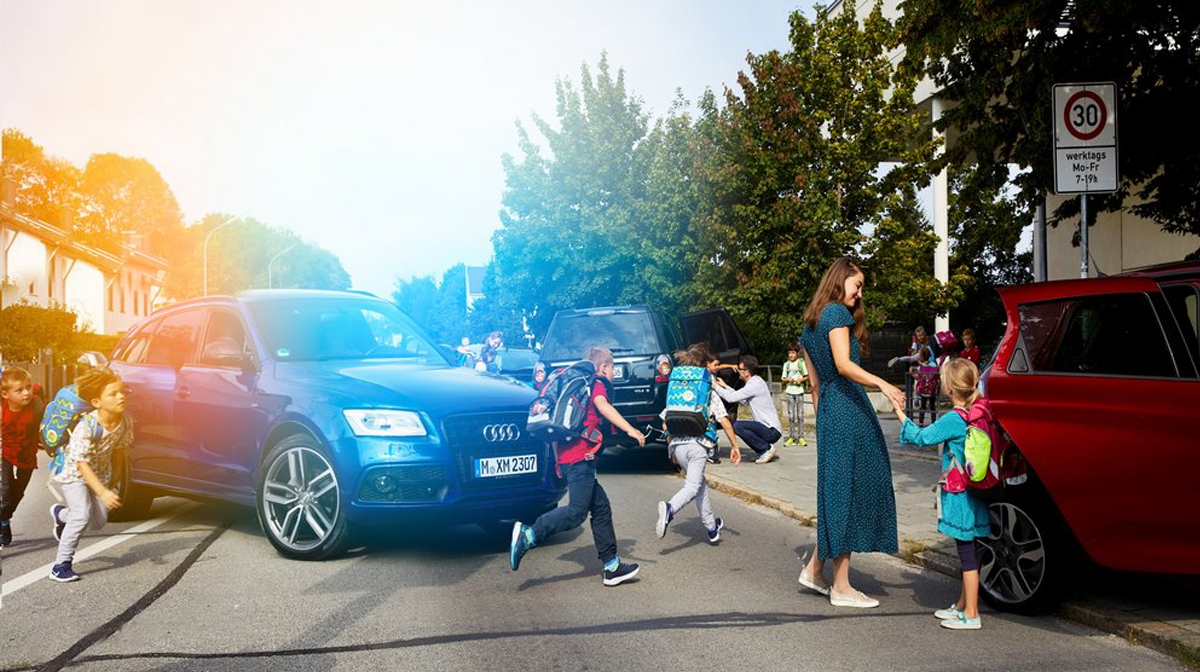 Das Bild zeigt ein Verkehrschaos vor einer Grundschule. Kinder laufen inmitten von Autos, die losfahren. Kinder steigen auf der Straßenseite aus dem Auto aus.