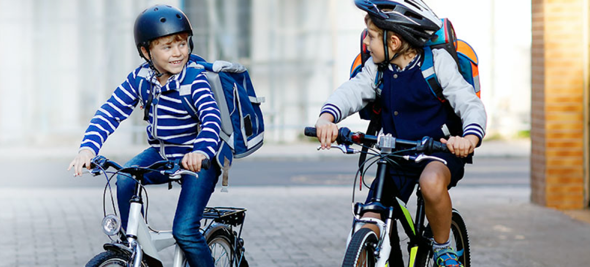 Zwei Jungen fahren nebeneinander Fahrrad und unterhalten sich. Sie tragen Helme.