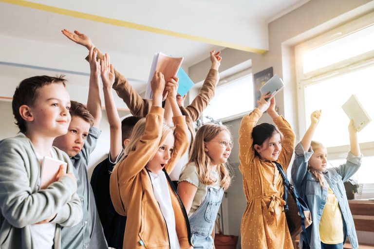 Freudige Kinder in einem Klassenraum, die Hände nach oben gestreckt