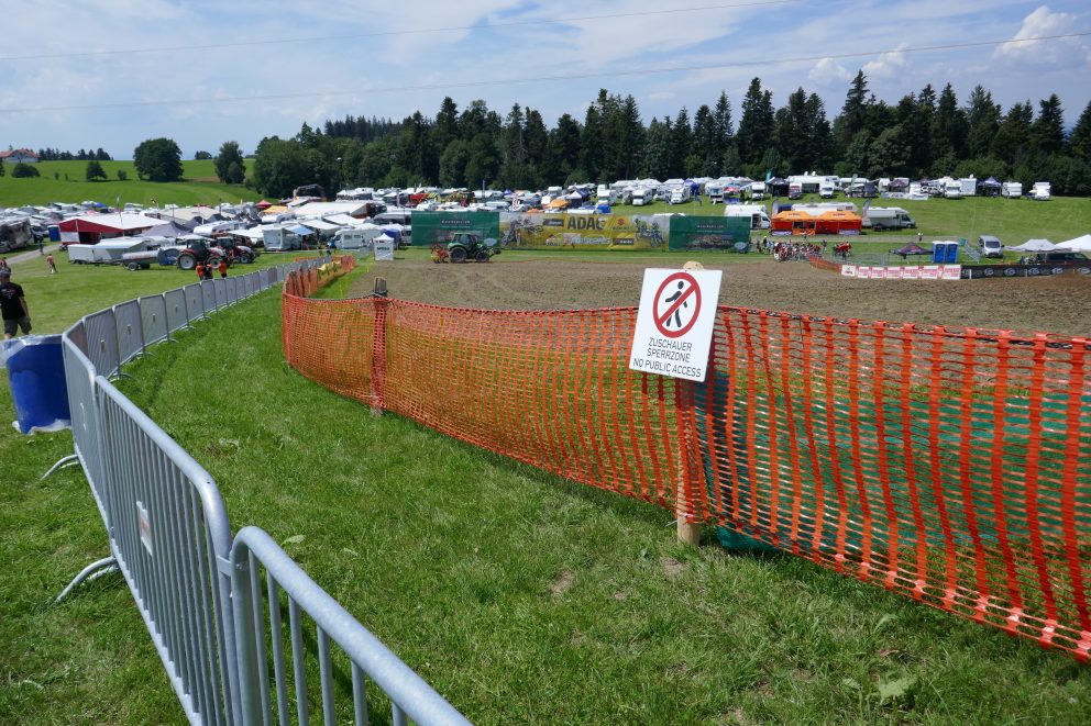 Absperrung an einer Motorradrennstrecke, Strecke und Parkplatz im Hintergrund.