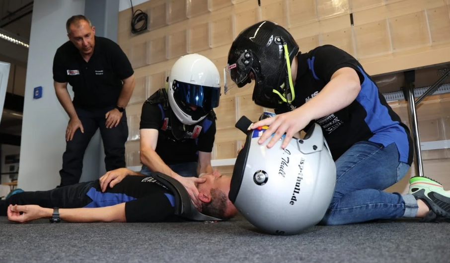 Erste Hilfe Schulung, 2 Personen mit einem Motorradhelm übern erste Hilfe an einer auf dem Boden liegenden Personen.