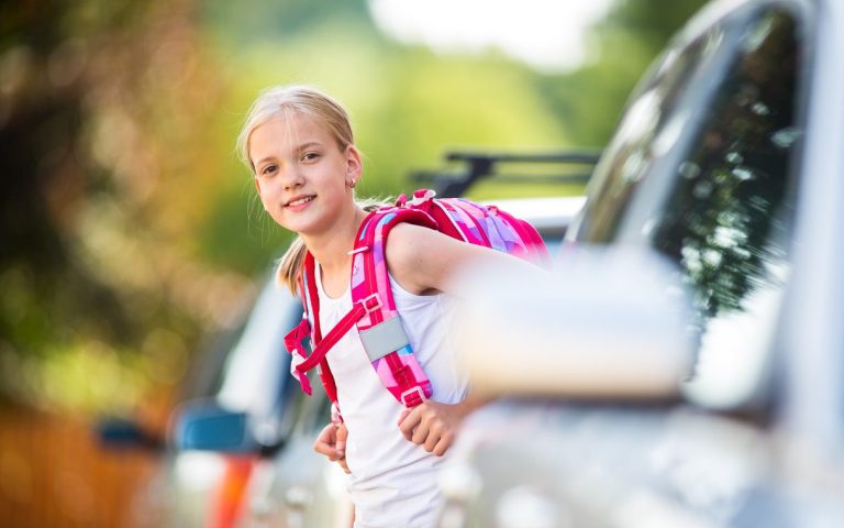 Ein Mädchen auf dem Heimweg nach der Schule. Sie geht zu Fuß und schaut zwischen parkenden Autos hervor.