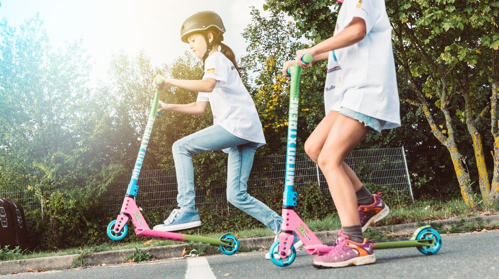 Zwei Mädchen fahren auf ihrem Roller nebeneinander.