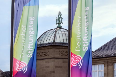 Flaggen mit Deutscher Stiftungstag Logo vor einem Gebäude außen.