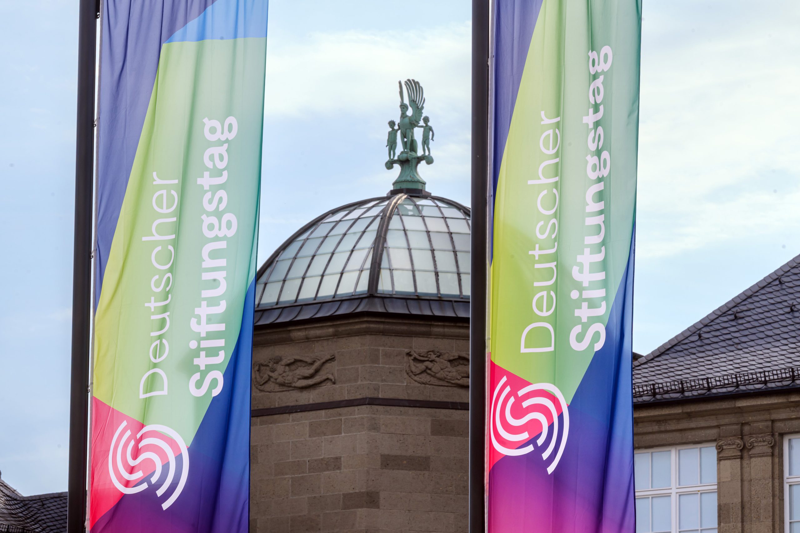 Flaggen mit Deutscher Stiftungstag Logo vor einem Gebäude außen.