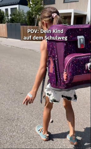 Ein Mädchen auf dem Schulweg, sie stößt einen Stein mit ihren Schuhen vor sich her.