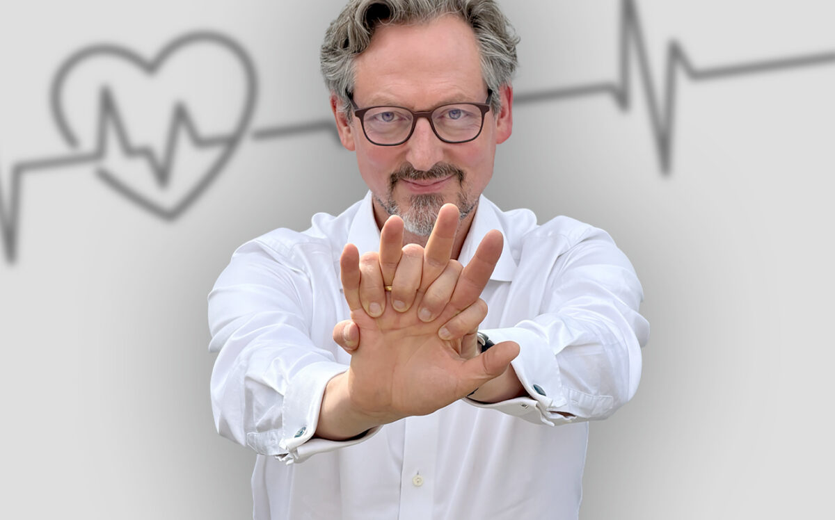 Porträt von Dr. Eckart von Hirschhausen mit nach vorne ausgestreckten Armen. Die übereinandergelegten Hände zeigen die Handhaltung für die Herzdruckmassage. Im Hintergrund sind ein stilisiertes Herz und eine Herzschlaglinie dargestellt.